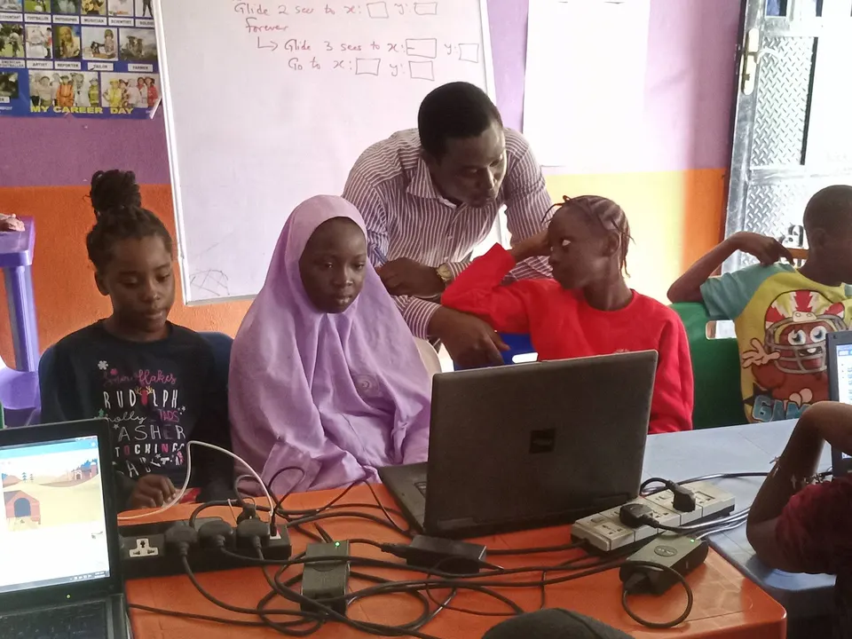 An instructor guiding girls working at laptops